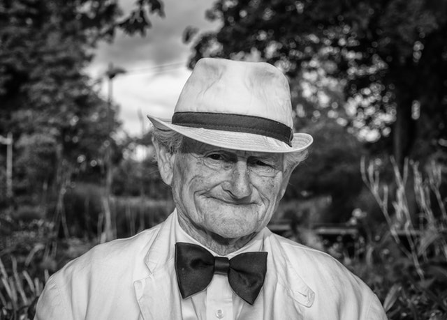 Starý pán v klobúku a s motýlikom sa usmieva.jpg